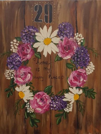 A circular floral wreath with pink roses, daisies, and purple flowers on a wooden background.