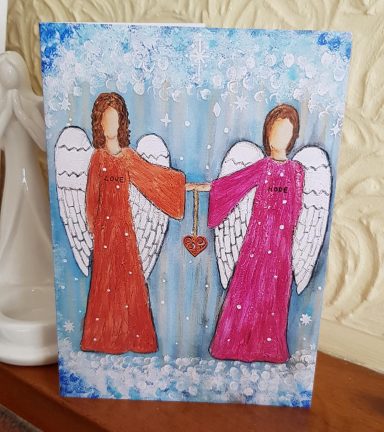 Two angels in red and pink dresses holding a small red heart against a blue background.