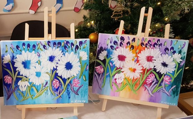 Two canvases with vibrant floral paintings featuring daisies on easels.
