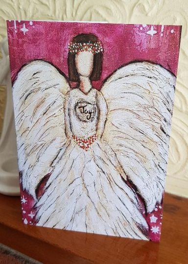 Angel with large white wings, wearing a flowing dress and a floral crown against a pink background.