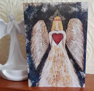 A hand-painted angel figure with a heart centre, draped in a flowing gown, against a dark backdrop.